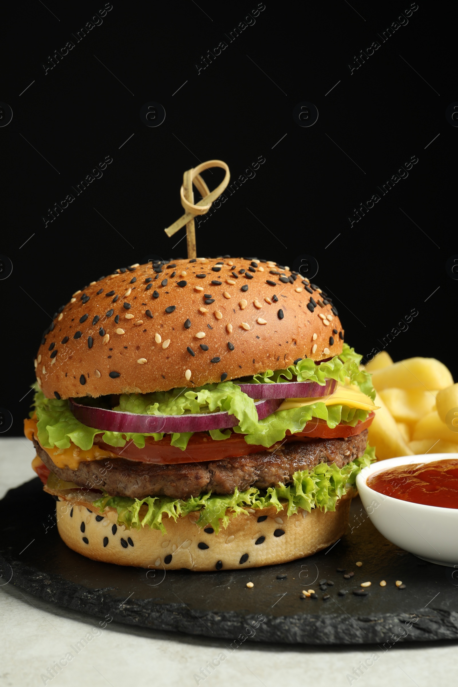 Burger with delicious patty, french fries and sauce on gray table against black background Photo of Burger with delicious patty, french fries and sauce on gray table against black background