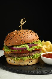 Photo of Burger with delicious patty, french fries and sauce on gray table against black background