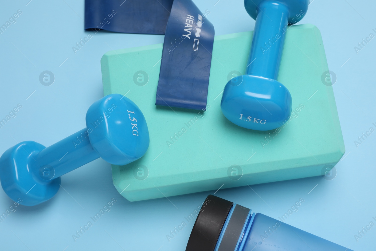 Photo of Two dumbbells, yoga block, fitness elastic band and bottle on light blue background, above view