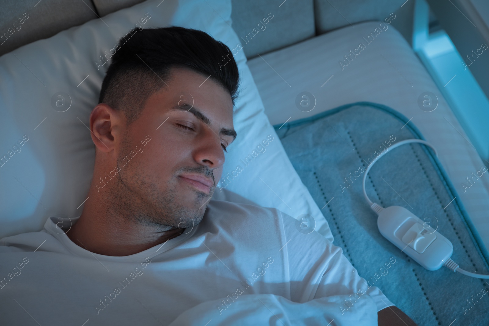 Photo of Man sleeping on electric heating pad in bed at night, above view