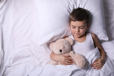 Photo of Little boy sleeping with teddy bear at home, top view. Bedtime