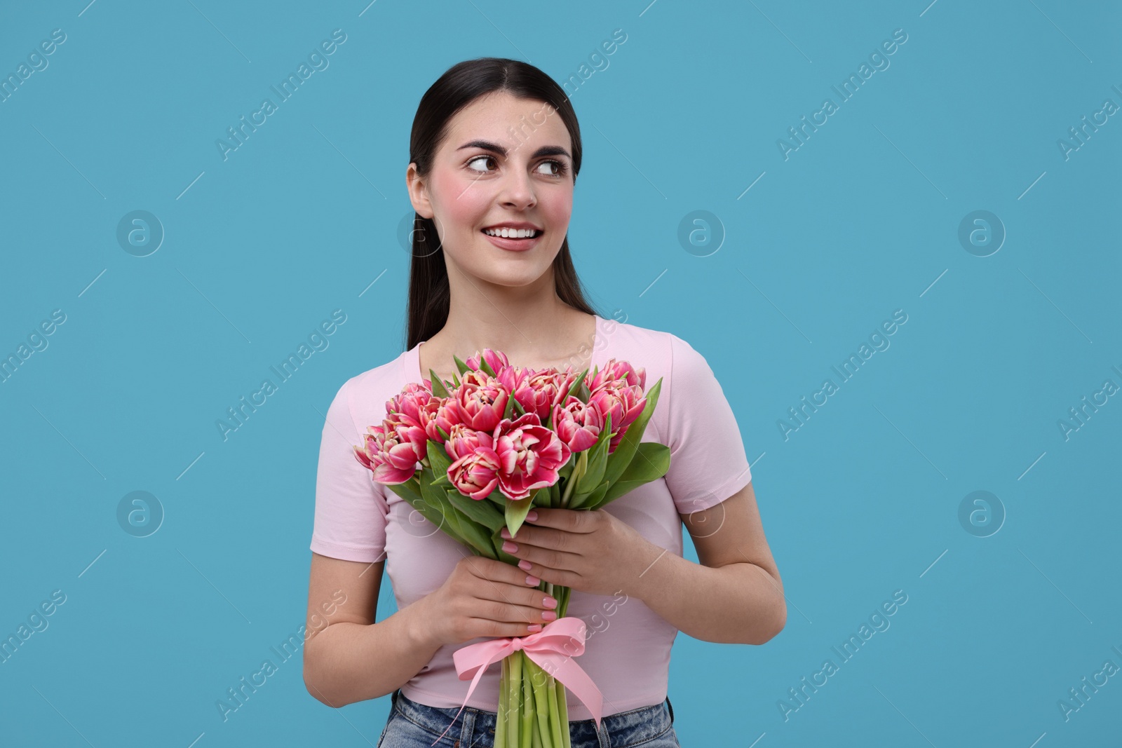 Photo of Happy young woman with beautiful bouquet on light blue background