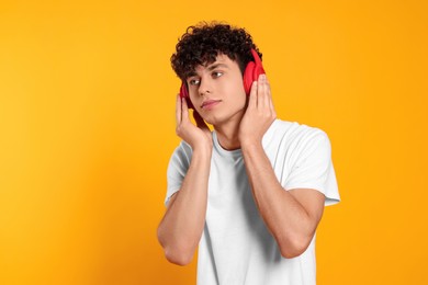 Handsome young man listening to music with headphones on orange background