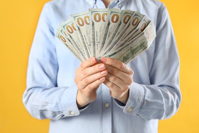 Woman holding dollar banknotes on yellow background, closeup. Money exchange concept