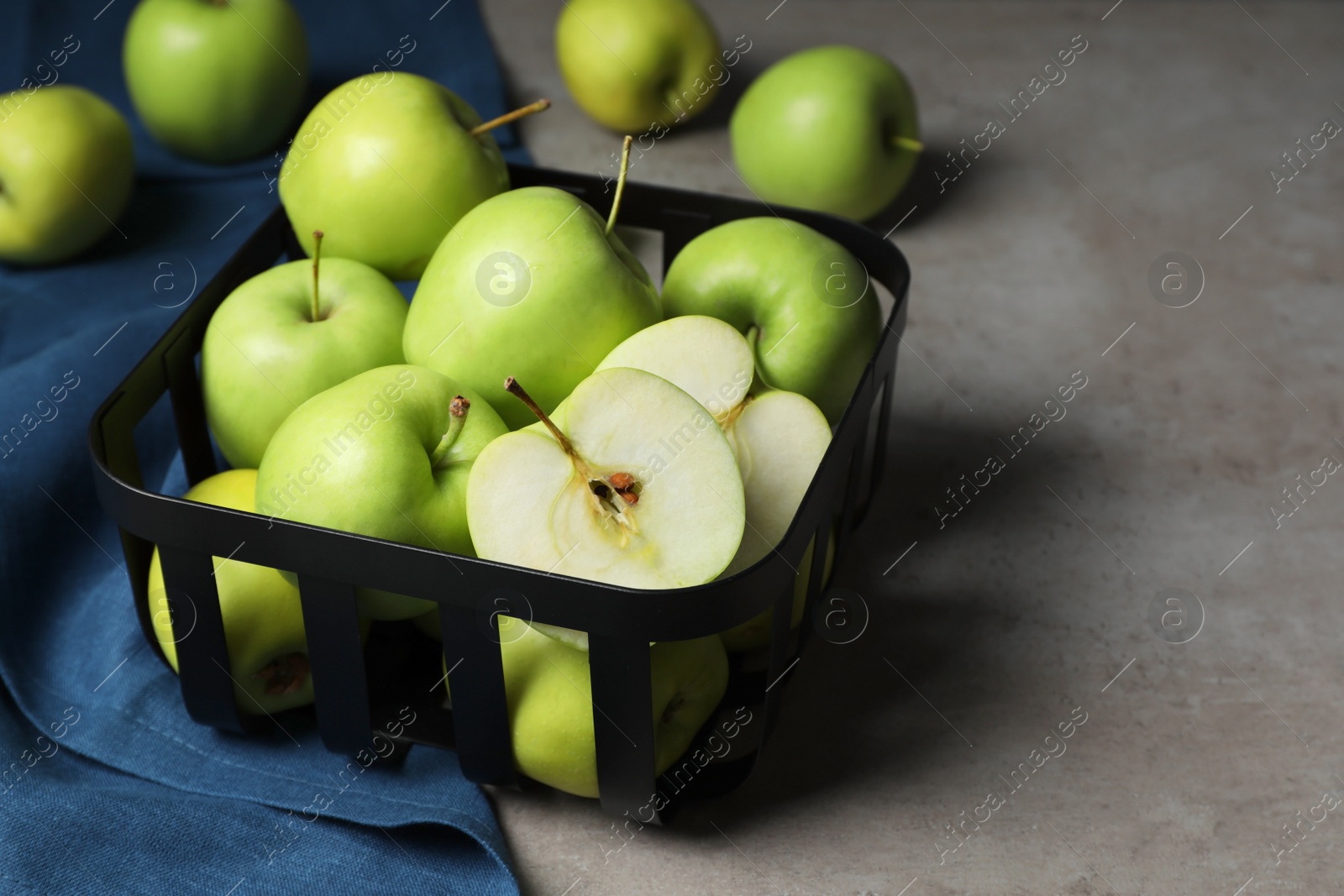 Photo of Black metal container full of apples on grey table, closeup