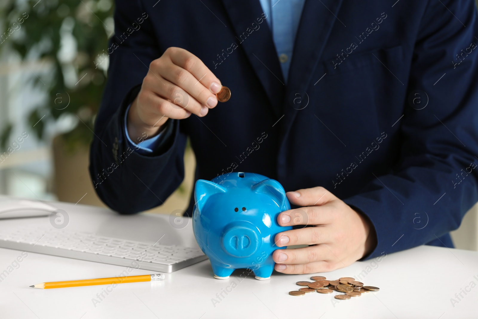 Photo of Man putting coin into piggy bank at white table, closeup. Money savings