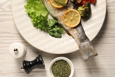 Photo of Delicious baked fish and vegetables served on wooden table, flat lay