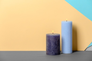 Photo of Decorative wax candles on table against color background