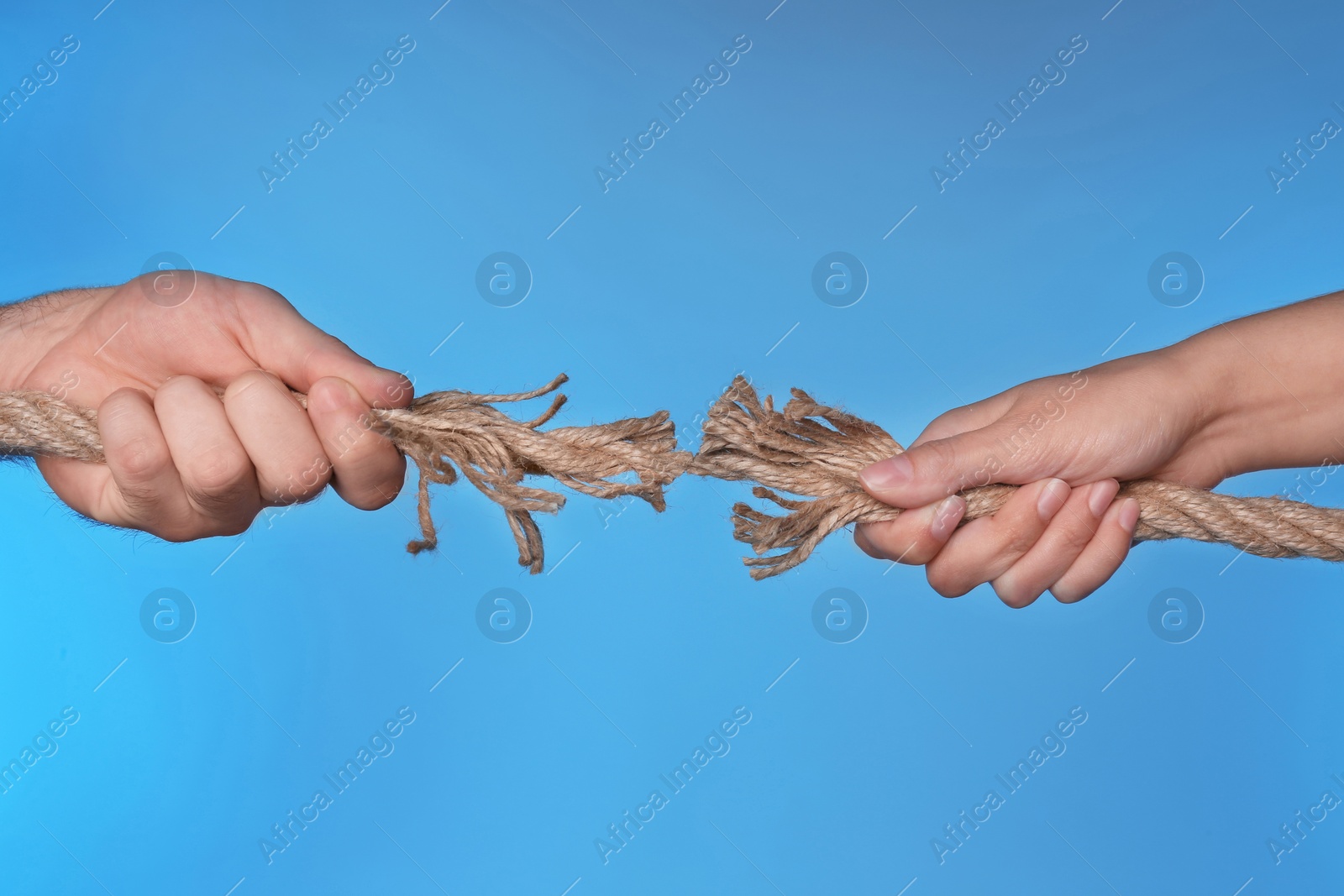 Photo of Woman and man pulling damaged rope on color background, closeup