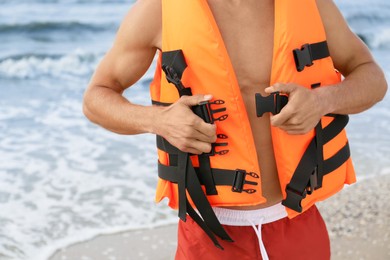 Lifeguard putting on life vest near sea, closeup