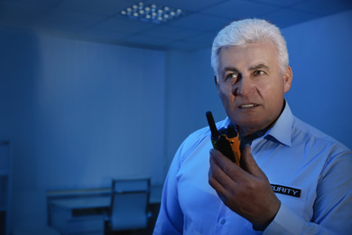 Professional security guard with portable radio set in dark room
