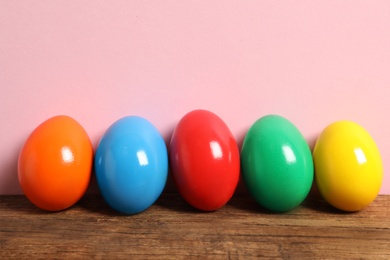 Photo of Easter eggs on wooden table against pink background