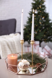 Burning candles and fir branch on table in room decorated for Christmas