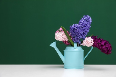 Photo of Beautiful hyacinths in watering can on table against color background, space for text. Spring flowers