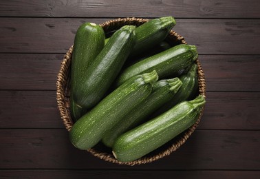 Photo of Raw ripe zucchinis in wicker bowl on wooden table, top view