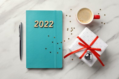 Photo of Turquoise planner, cup of coffee and gift box on white marble background, flat lay. 2022 New Year aims