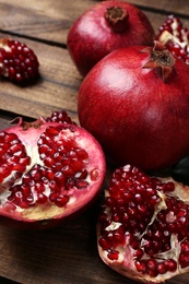 Photo of Delicious red ripe pomegranates on wooden background, closeup