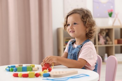 Photo of Motor skills development. Little girl playing with wooden pieces and string for threading activity at table indoors