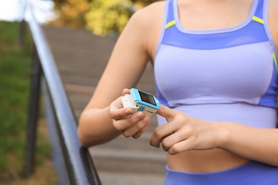 Photo of Woman checking pulse with blood pressure monitor on finger after training outdoors, closeup. Space for text