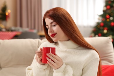 Photo of Beautiful young woman with cup of tea on sofa at home, space for text. Celebrating Christmas
