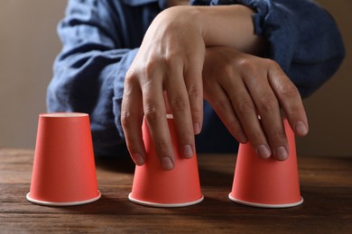 Photo of Woman playing thimblerig game with red cups at wooden table, closeup
