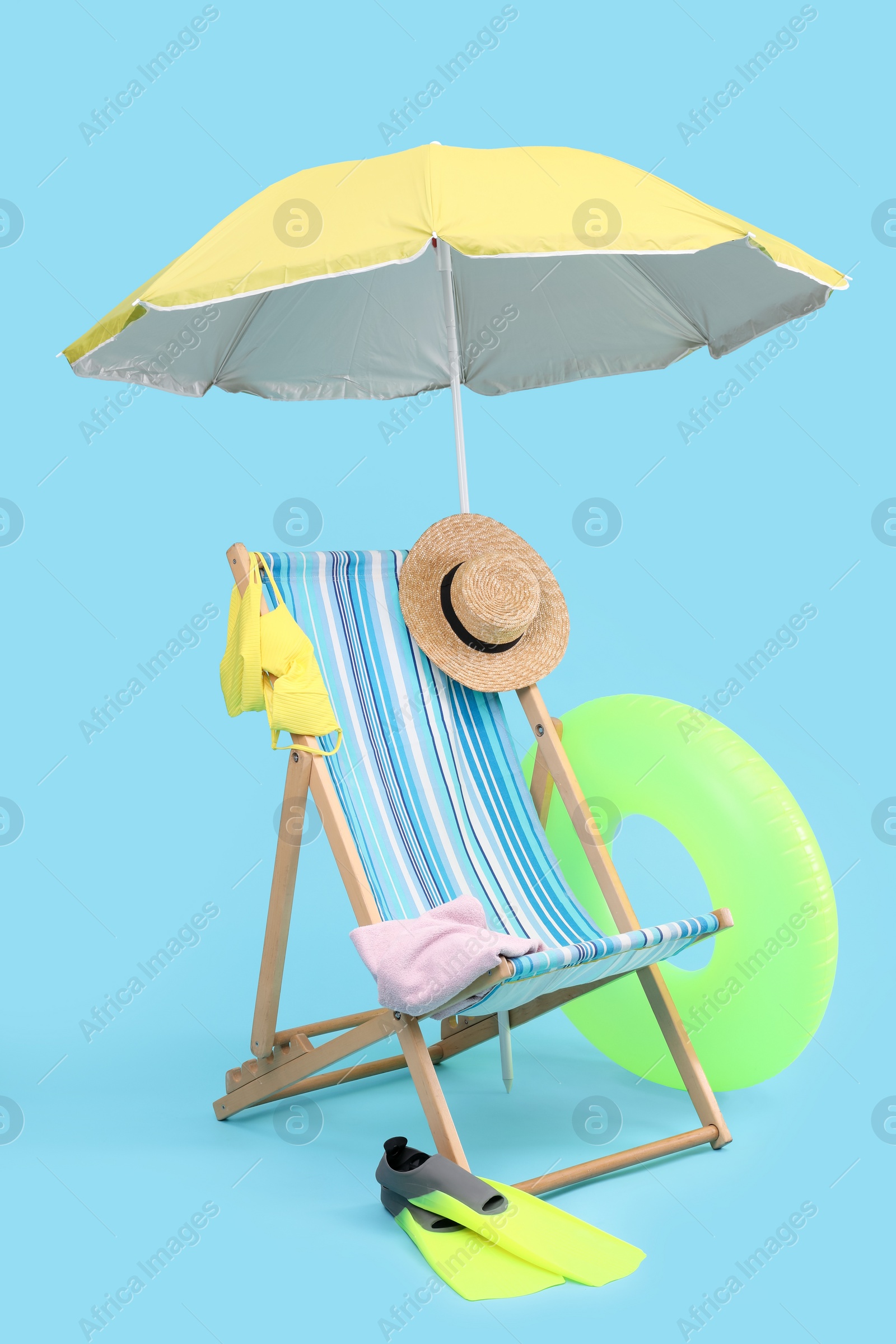 Photo of Deck chair, umbrella and beach accessories against light blue background. Summer vacation