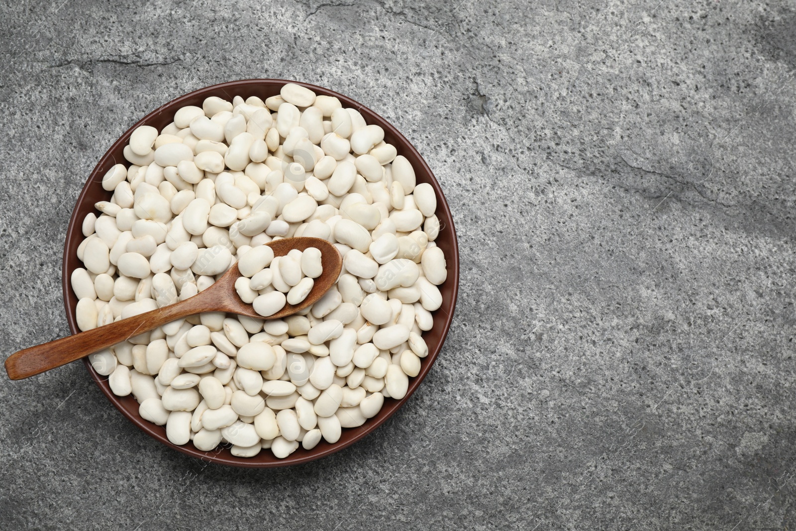Photo of Raw white beans and spoon in bowl on wooden table, top view. Space for text