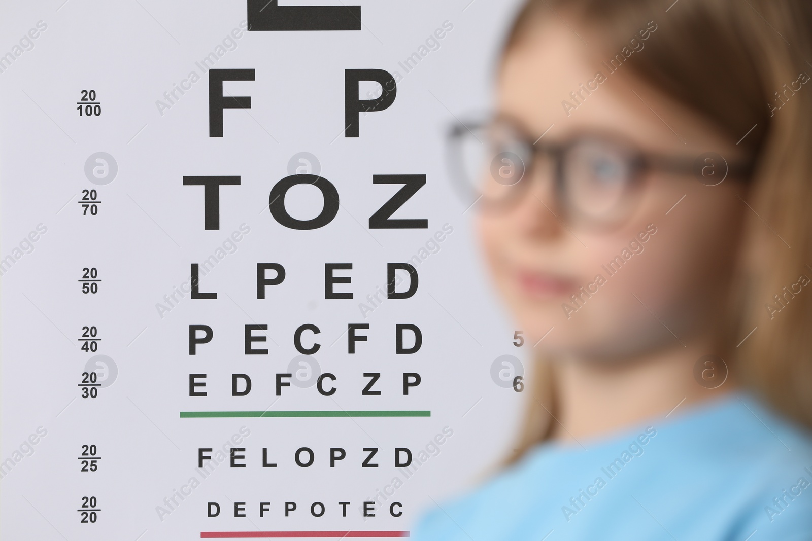 Photo of Little girl with glasses against vision test chart, selective focus