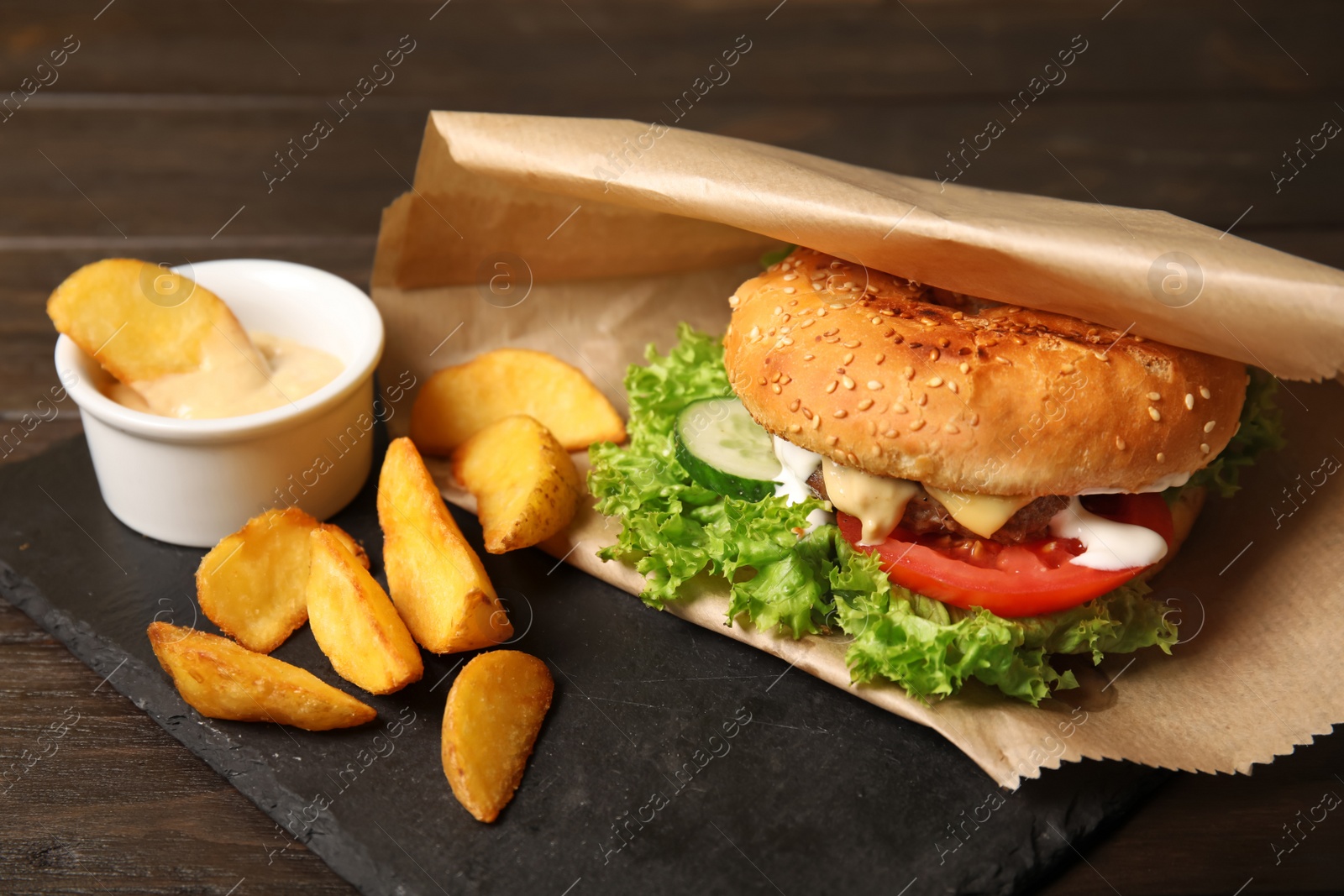 Photo of Tasty burger and fries served on slate plate, closeup