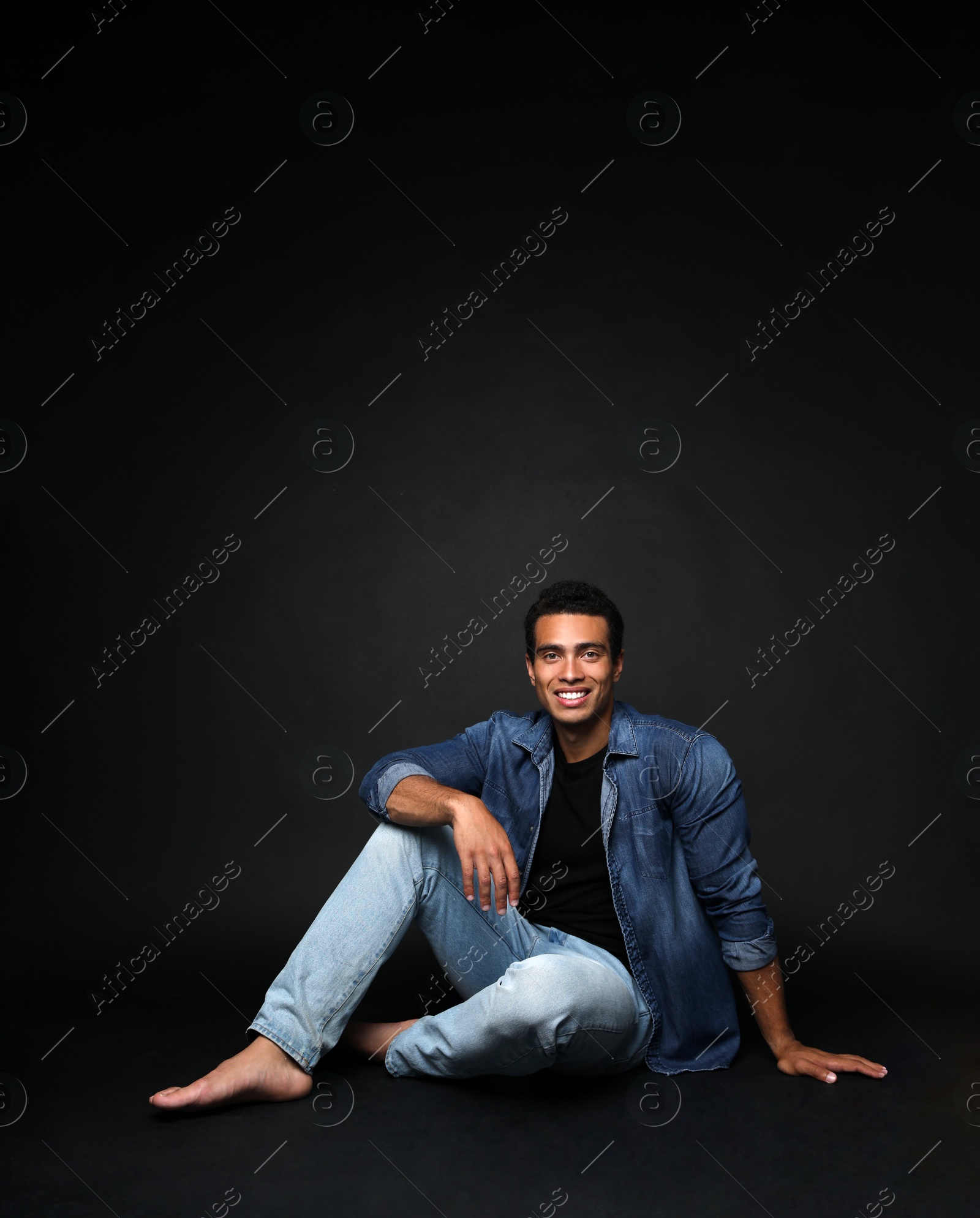 Photo of Handsome young African-American man sitting on black background