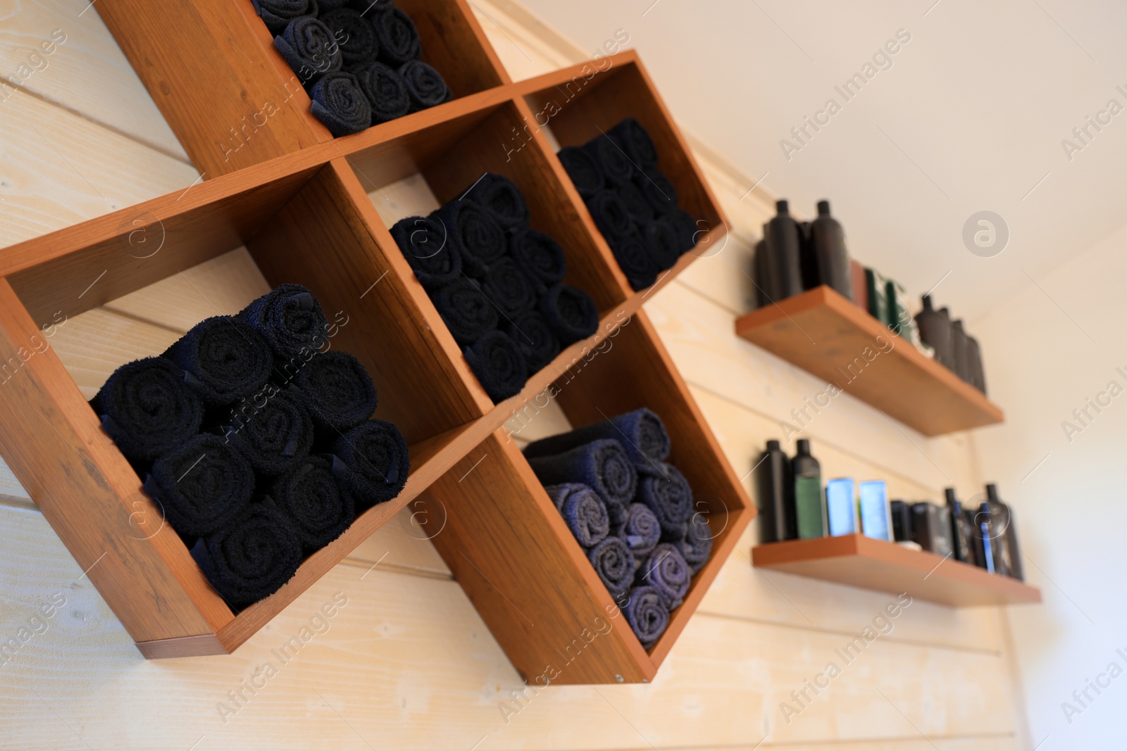 Photo of Shelves with rolled towels and professional hair cosmetics on wall in barbershop, closeup