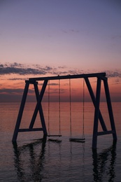 Photo of Picturesque view of swing in water on sunrise