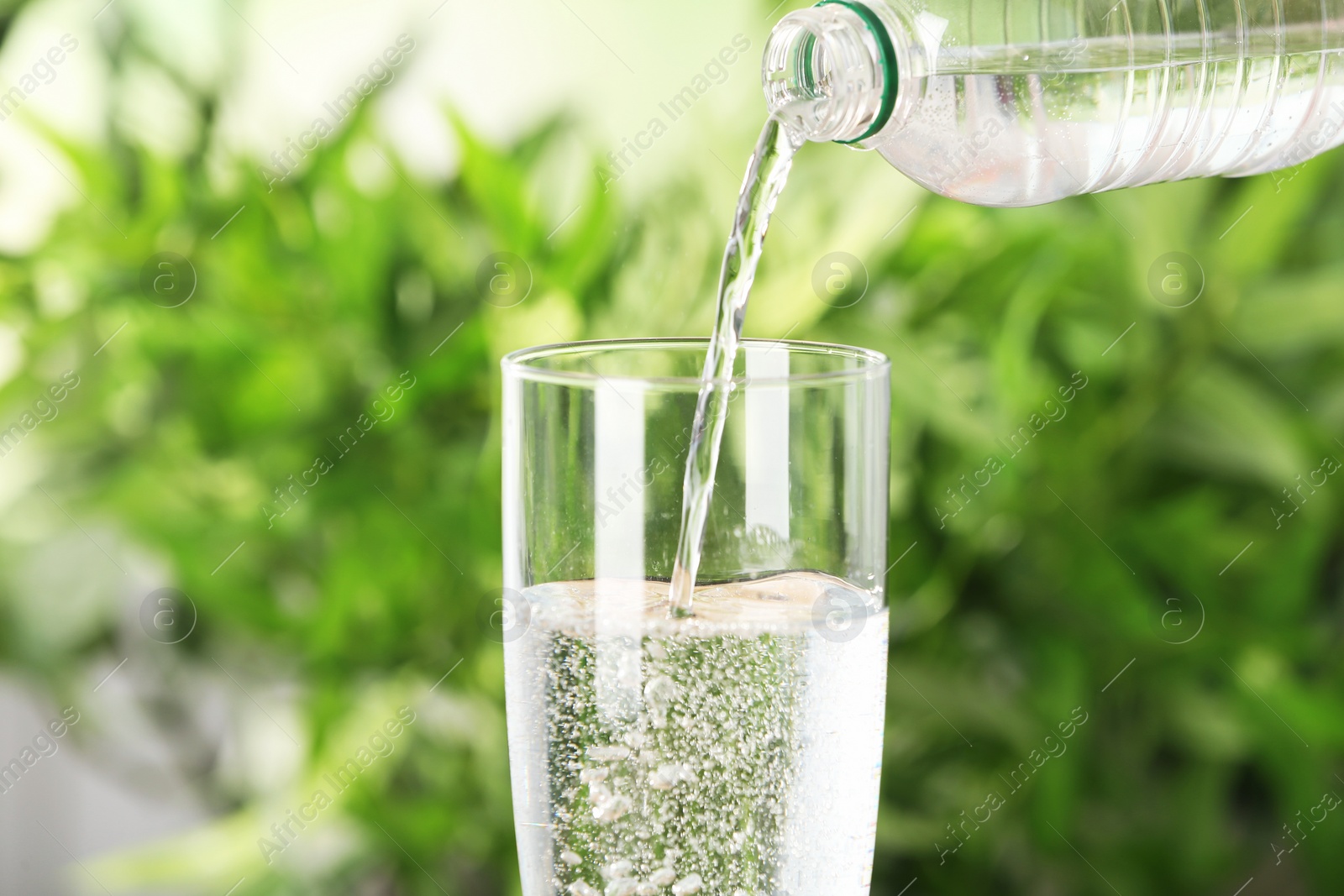 Photo of Pouring water from bottle into glass on blurred background