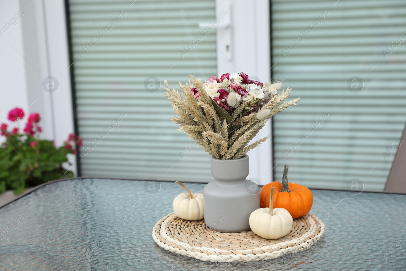 Photo of Beautiful bouquet of dry flowers and small pumpkins on glass table outdoors