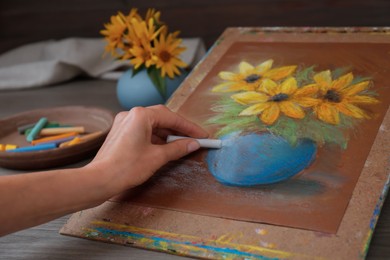 Photo of Woman drawing beautiful flowers in vase on paper with pastel at table, closeup