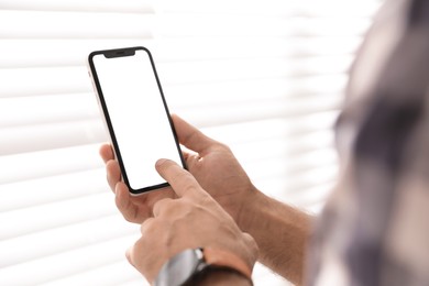 Photo of Man using mobile phone with empty screen near window indoors, closeup