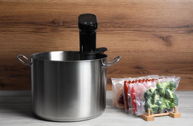 Sous vide cooking. Thermal immersion circulator in pot and vacuum packed food products on white wooden table