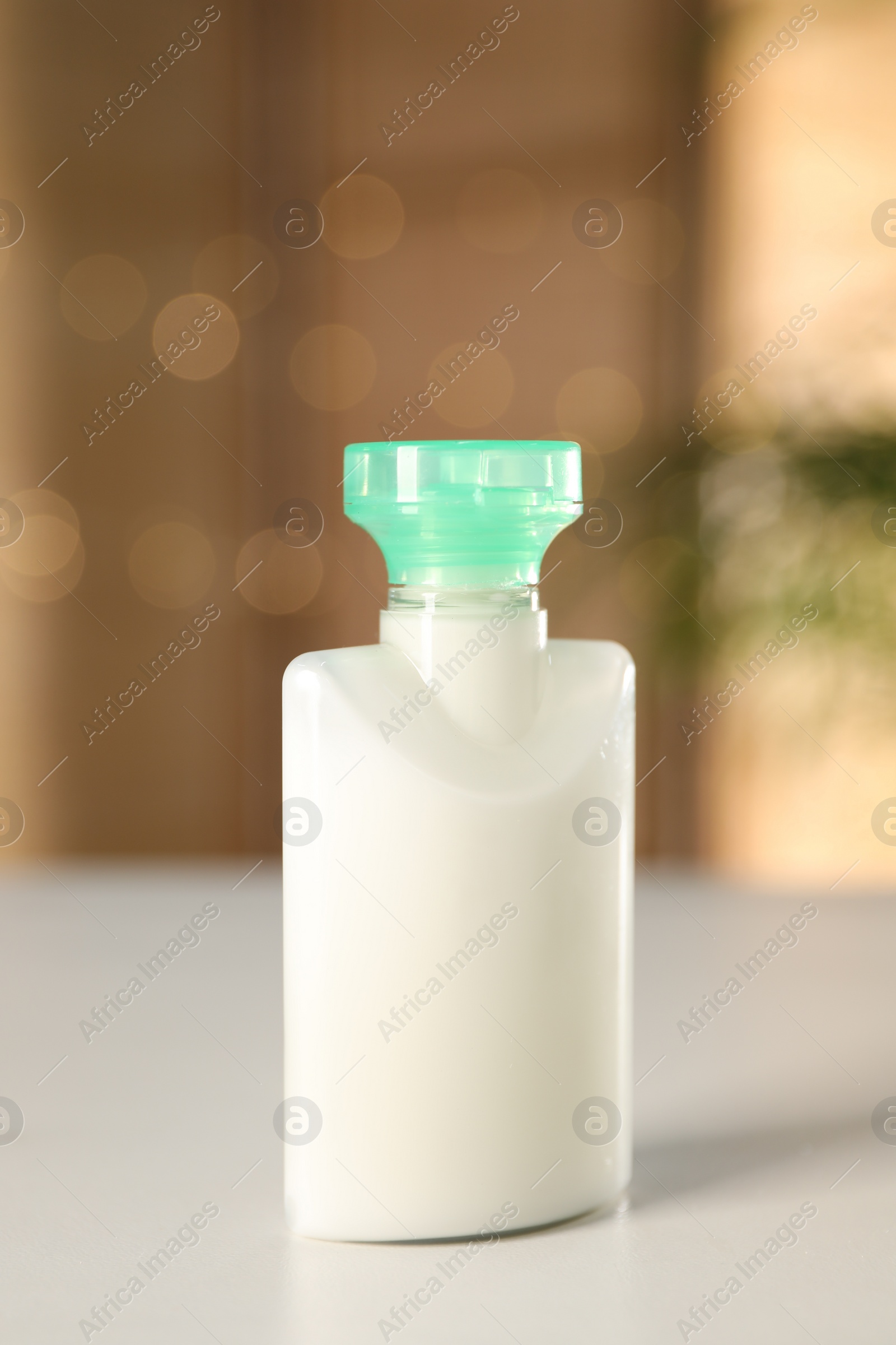 Photo of Mini bottle of cosmetic product on white table against blurred background