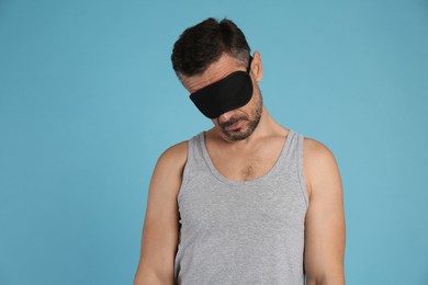 Man with eye mask in sleepwalking state on light blue background