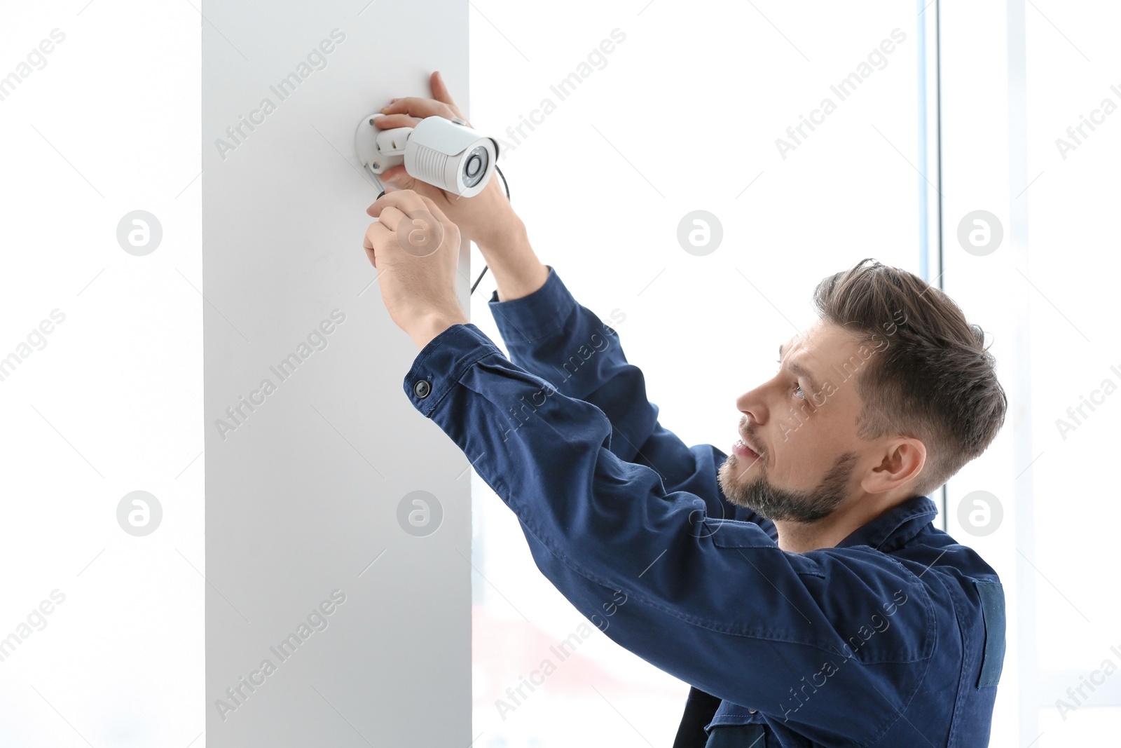 Photo of Technician installing CCTV camera on wall indoors