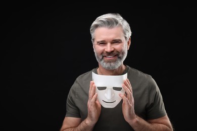 Multiple personality concept. Happy man with mask on black background