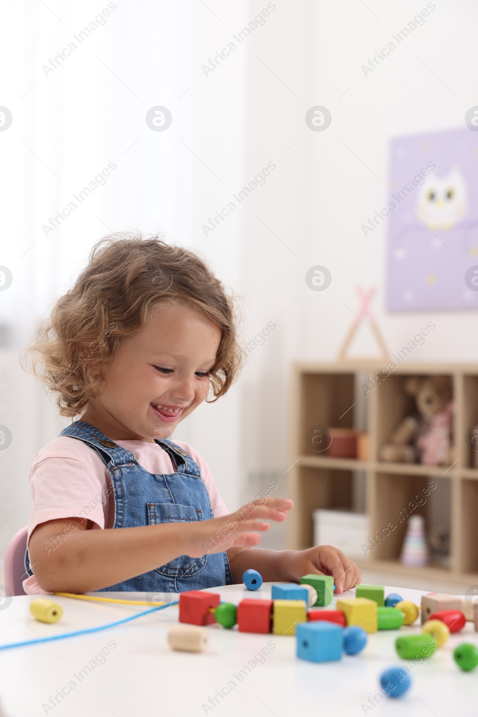 Photo of Motor skills development. Little girl playing with wooden pieces and string for threading activity at table indoors