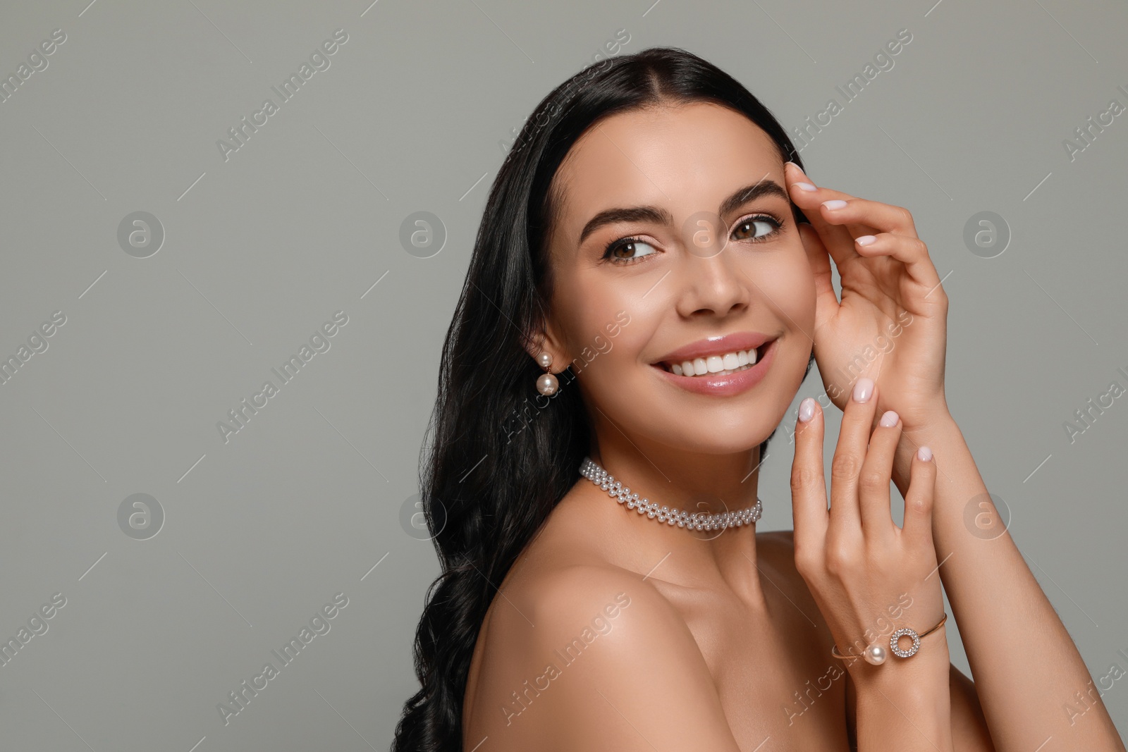 Photo of Young woman wearing elegant pearl jewelry on grey background, space for text