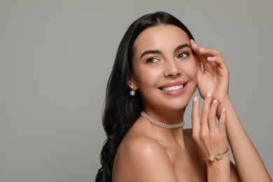 Young woman wearing elegant pearl jewelry on grey background, space for text