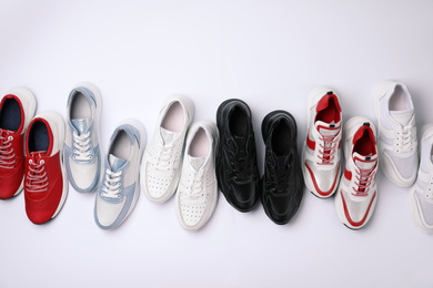 Many stylish sneakers on white background, top view