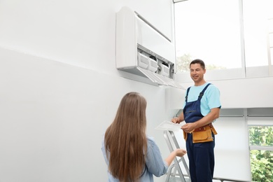 Photo of Technician speaking with woman while cleaning air conditioner indoors