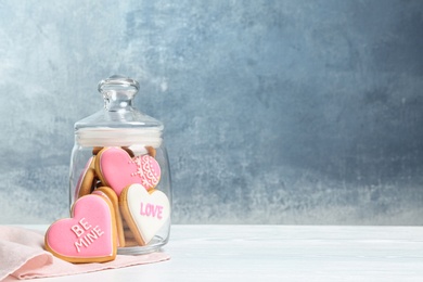 Photo of Decorated heart shaped cookies in glass jar on table. Space for text