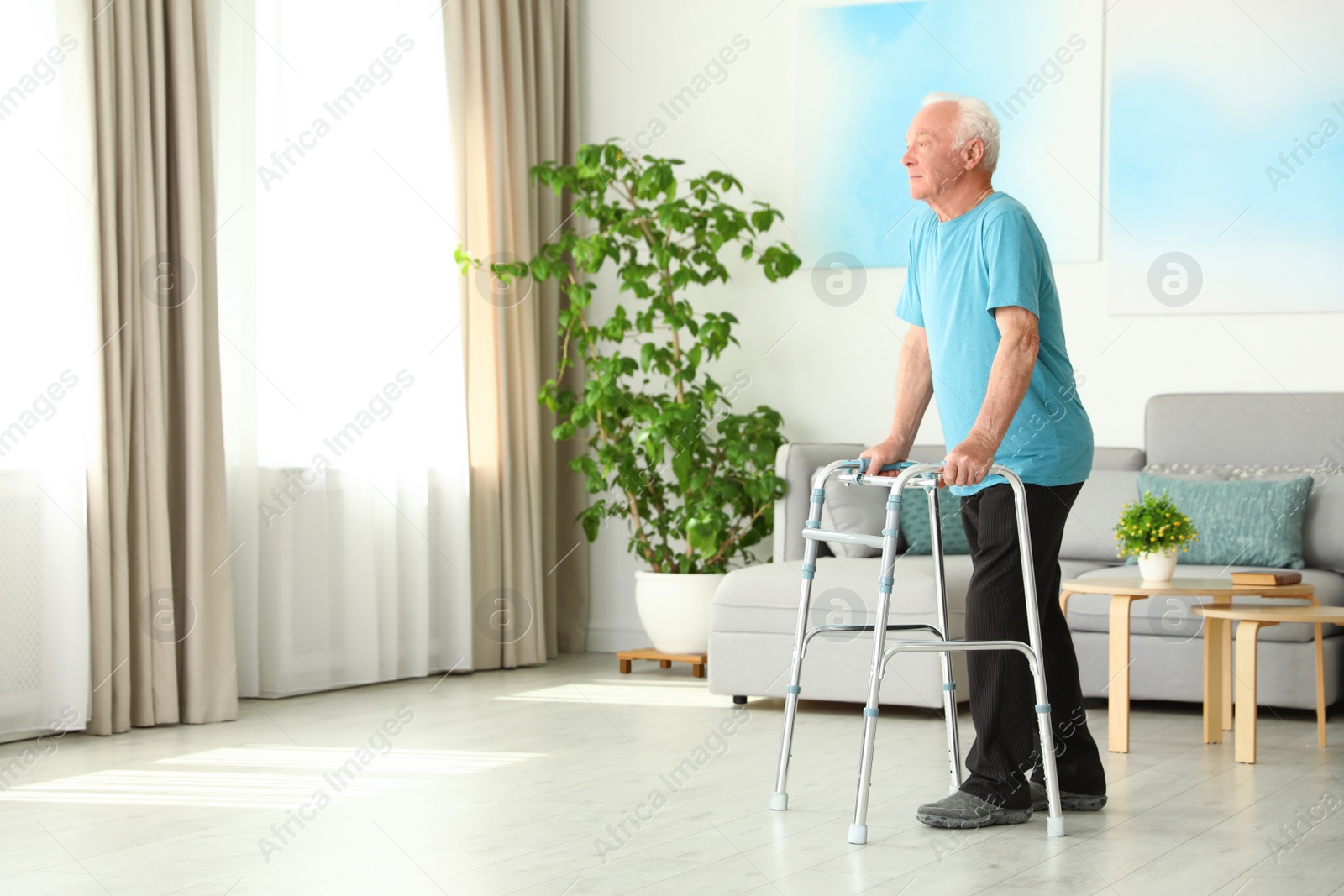 Photo of Elderly man using walking frame indoors. Space for text