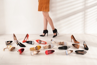 Photo of Woman trying on different high heel shoes near light wall, closeup