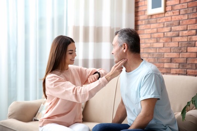 Young woman checking mature man's pulse with fingers at home